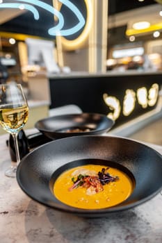 Pumpkin cream soup with shrimp on the table in a restaurant with a glass of wine. High quality photo