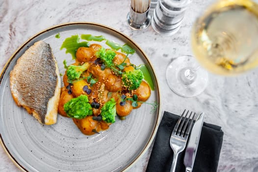 Sea bass or dorado fillet with baked potatoes and cauliflower on a gray plate on a marble table in a restaurant