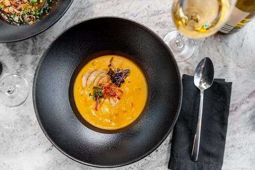 Pumpkin cream soup with shrimp on the table in a restaurant with a glass of wine. High quality photo