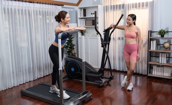 Energetic and strong athletic asian woman running on elliptical running machine at home with workout buddy or trainer. Pursuit of fit physique and commitment to healthy lifestyle. Vigorous