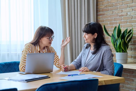 Two mature business women colleagues employees working together in office, middle-aged females preparing contract financial legal plan. Work professionals teamwork communication 40s 50s people on job