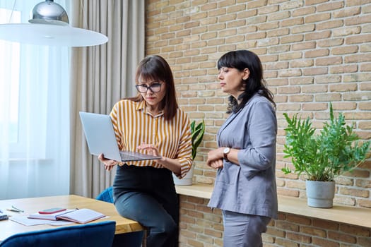 Two mature business women colleagues employees working together in office, middle-aged females preparing contract financial legal plan. Work professionals teamwork communication 40s 50s people on job