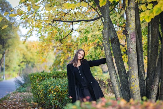 A beautiful girl stands by a tree in an autumn park