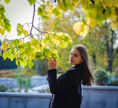 A beautiful girl looks at yellow leaves on a branch in an autumn park