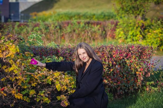 Portrait of a beautiful girl near a red-yellow bush in an autumn park