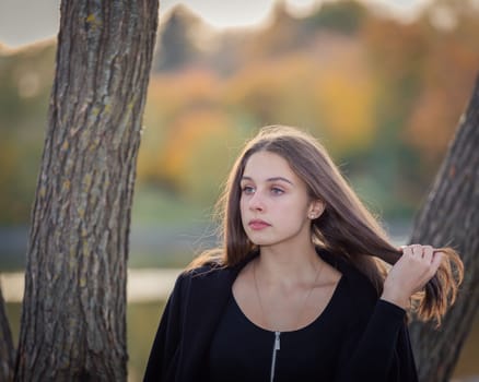 A beautiful girl poses while standing by a pond in an autumn park