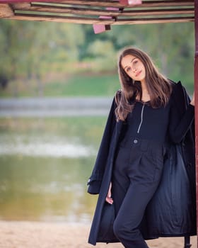 A beautiful girl poses while standing by a pond under an umbrella in an autumn park