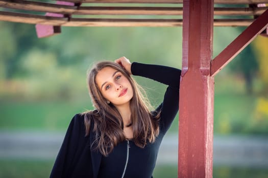 A beautiful girl poses while standing by a pond under an umbrella in an autumn park