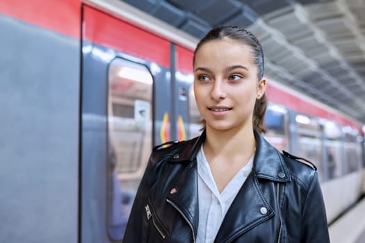 Teenage girl on platform of subway station, against backdrop of subway train. Student teenager youth, lifestyle in city, subway passengers, urban transport concept