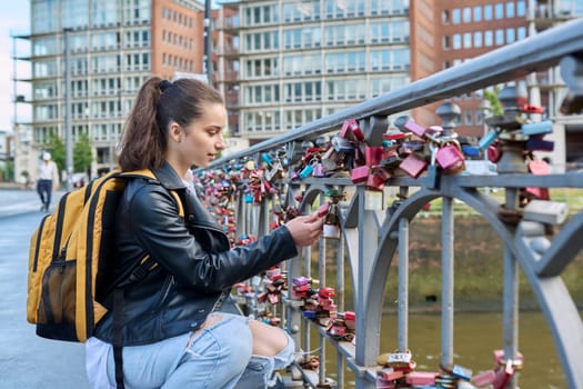 Young teenage girl touches closed love lock on bridge. Romantic signs symbols, love relationships people concept