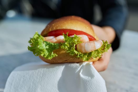 Traditional street sea food, shrimp burger, close-up in outdoor hands.