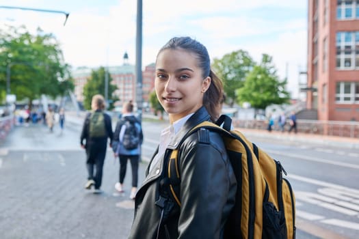 Portrait of teenage high school student, smiling confident girl 16, 17 years old with backpack looking at camera outdoor, on street of modern city. Urban life, adolescence, education, youth concept