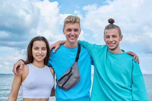 Portrait of cheerful teenage friends hugging outdoor, happy young people posing looking at camera on beach. Youth, team, summer vacation, communication, leisure, friendship, fun, lifestyle, holiday