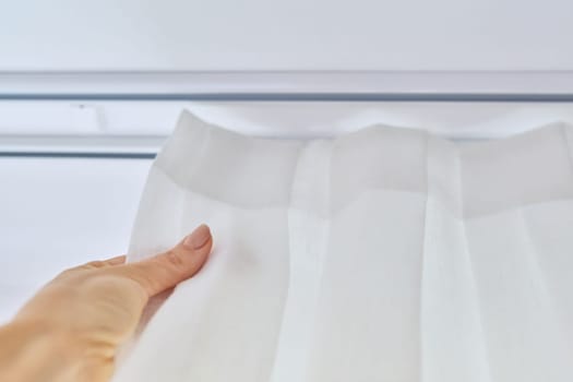 Translucent white textured curtain on window, close-up of ceiling cornice and fabric gathered on braid, laid and sewn with decorative folds, on plastic hooks