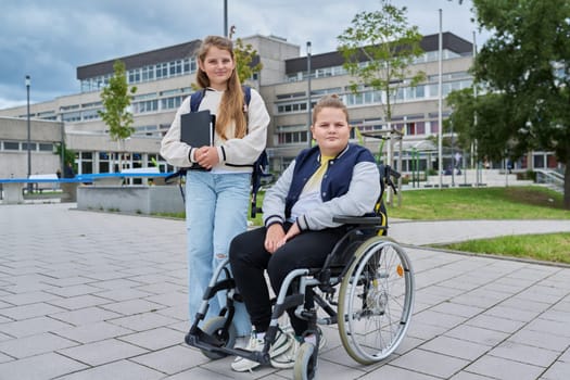 Portrait of classmates friends 10, 11 years old, boy in wheelchair and girl looking at camera, outdoor near school building. Education, friendship, communication, disability, inclusiveness