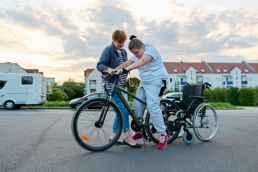 Boy transfers from wheelchair to bicycle, mother helping child to transfer, activity rehabilitation health concept