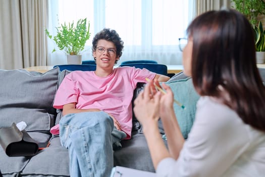 Young male having mental therapy in psychologist's office. Guy college student talking to therapist, female counselor listening talking making clipboard notes. Support psychology psychotherapy concept