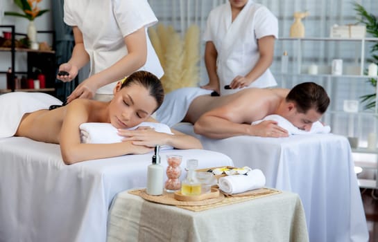 Hot stone massage at spa salon in luxury resort with day light serenity ambient, blissful couple customer enjoying spa basalt stone massage glide over body with soothing warmth. Quiescent