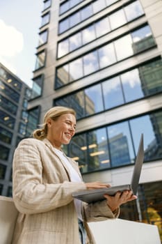 Focused smiling business woman working laptop on modern building background
