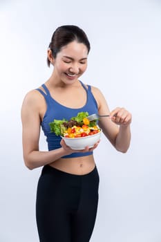 Young sporty Asian woman in sportswear holding salad bowl fill with vibrant of fruit and vegetable. Natural youthful and fit body lifestyle with balance nutrition on isolated background. Vigorous