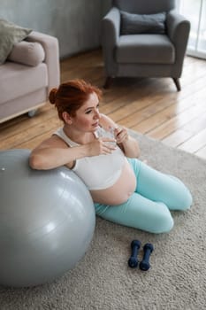 Pregnant woman drinks water after workout on fitness ball