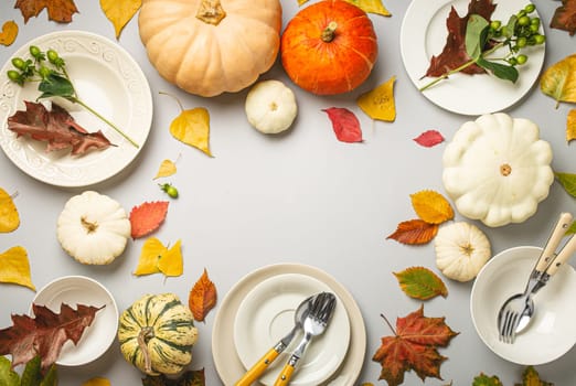 Thanksgiving festive table composition with different colourful pumpkins, autumn leaves, empty plates with cutlery on light grey background table ready for party and celebration. Space for text..
