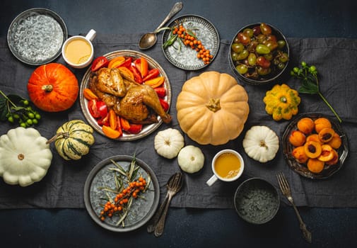 Thanksgiving festive table composition with roasted turkey, pumpkins, vegetable salad, fruit, orange beverage. Thanksgiving celebration dinner with traditional autumn meals on rustic dark table.