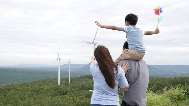 Concept of progressive happy family enjoying their time at the wind turbine farm. Electric generator from wind by wind turbine generator on the country side with hill and mountain on the horizon.