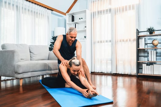 Happy active senior couple in sportswear being supportive and assist on yoga posture together at home. Healthy senior man and woman lifestyle with yoga exercise. Clout