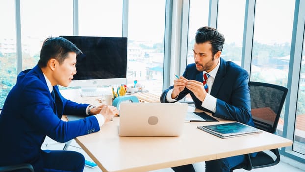 Two business people talk project strategy at office meeting room. Businessman discuss project planning with colleague at modern workplace while having conversation and advice on financial report. Jivy