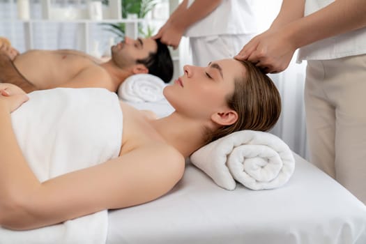 Caucasian couple enjoying relaxing anti-stress head massage and pampering facial beauty skin recreation leisure in dayspa modern light ambient at luxury resort or hotel spa salon. Quiescent