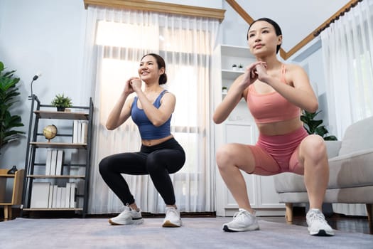 Vigorous energetic woman with trainer or workout buddy doing exercise at home. Young athletic asian woman strength and endurance training session as home workout routine with squat.