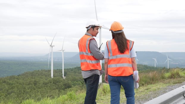 Male and female engineers working on a wind farm atop a hill or mountain in the rural. Progressive ideal for the future production of renewable, sustainable energy.