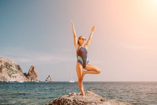 Woman sea yoga. Back view of free calm happy satisfied woman with long hair standing on top rock with yoga position against of sky by the sea. Healthy lifestyle outdoors in nature, fitness concept.