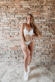A mid-30s happy woman with long hair natural color poses in her underwear, smiling in front of a brick wall on a construction site for model tests.