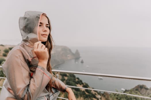 Woman rain park. Happy woman portrait wearing a raincoat with transparent umbrella outdoors on rainy day in park near sea. Girl on the nature on rainy overcast day