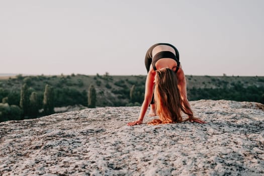 Well looking middle aged woman with long hair, fitness instructor in leggings and tops doing stretching and pilates on the rock near forest. Female fitness yoga routine concept. Healthy lifestyle.