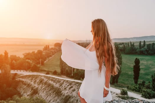 Romantic beautiful bride in white dress posing with sea and mountains in background. Stylish bride standing back on beautiful landscape of sea and mountains on sunset