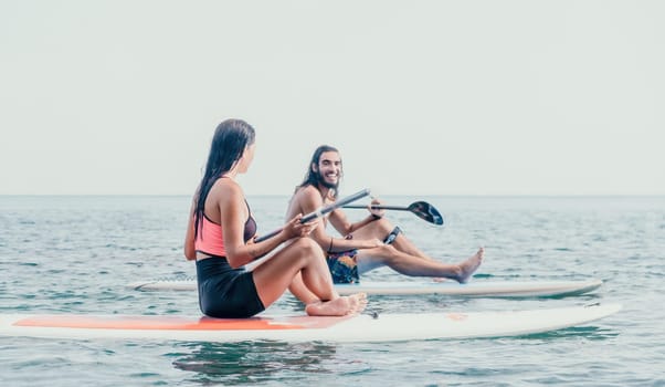 Woman man sup yoga. Happy young sporty couple practising yoga pilates on paddle sup surfboard. Female stretching doing workout on sea water. Modern family outdoor summer sport activity