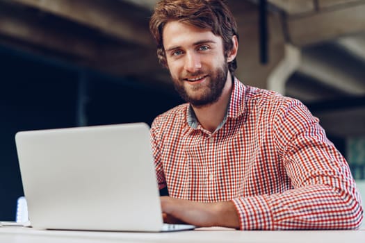 Portrait of young caucasian businessman using laptop computer at his workplace in modern office