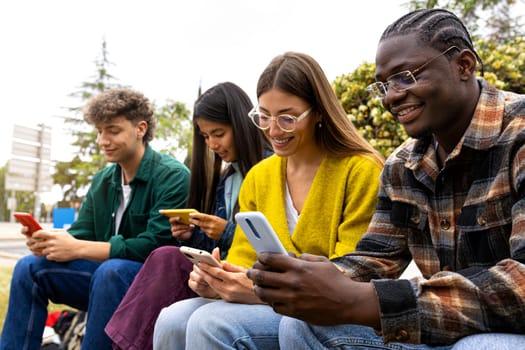 Group of multiracial teenage college friend students ignoring each other looking at mobile phone. Smartphone addiction. Youth lifestyle and social media concept.