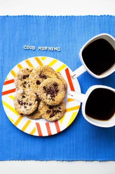 Oatmeal cookies with chocolate on blue napkin and two cups of coffee, good morning inscription