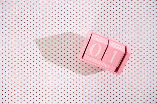 A pink block calendar displaying October 1st on a backdrop of red polka dots, casting a sharp shadow.