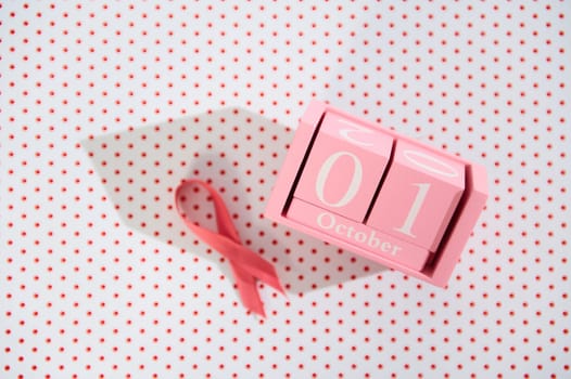 Pink ribbon and block calendar set to October 1st on polka dot background, symbolizing Breast Cancer Awareness Month.