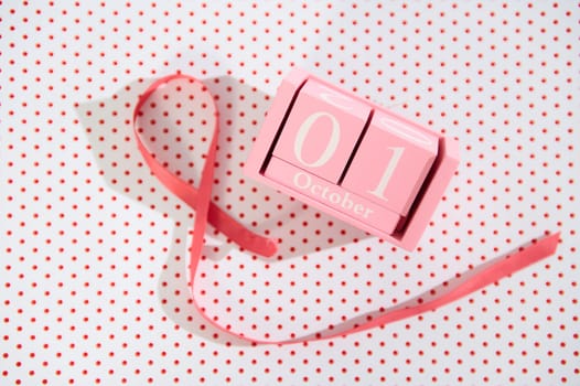 Pink cube calendar displaying October 1st, accompanied by a ribbon on a polka-dot background.