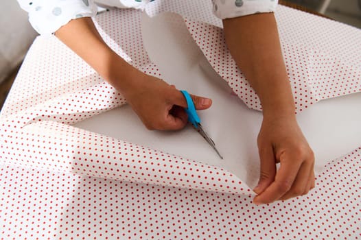 Hands using scissors to cut polka dot wrapping paper, crafting the perfect gift wrap for a special occasion.