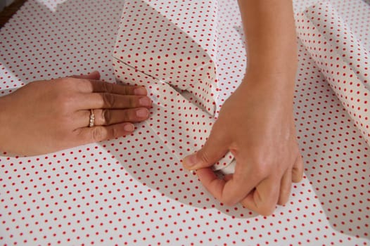 Close-up of hands skillfully wrapping a gift using red polka dot paper, capturing a moment of creativity and festive preparation.