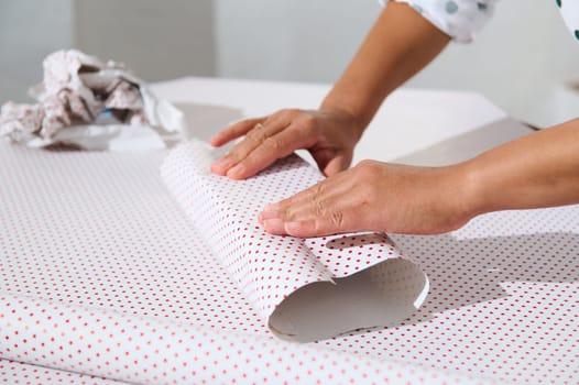 Close-up of hands wrapping a gift in polka dot paper, showcasing holiday preparation and creativity. Perfect for themes of gifting and celebrations.
