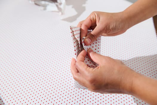 Close-up of hands carefully wrapping a gift with white paper adorned with red polka dots, embodying the festive spirit and attention to detail.