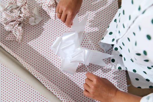 Close-up of hands carefully wrapping a gift with festive polka dot paper and a white ribbon, capturing the joy of gift-giving and celebration.